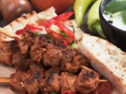 pork souvlaki on a wooden plate with vegetables and bread