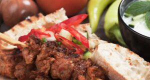 pork souvlaki on a wooden plate with vegetables and bread