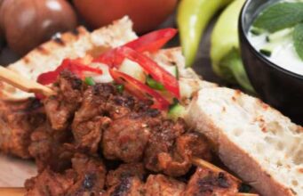 pork souvlaki on a wooden plate with vegetables and bread