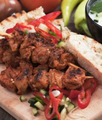 pork souvlaki on a wooden plate with vegetables and bread